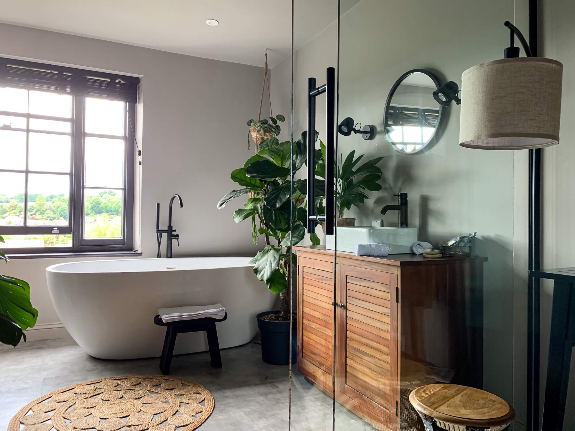 Modernt badrum med fristående badkar, svart blandare och träkommod – resultat av påkostad badrumsrenovering.